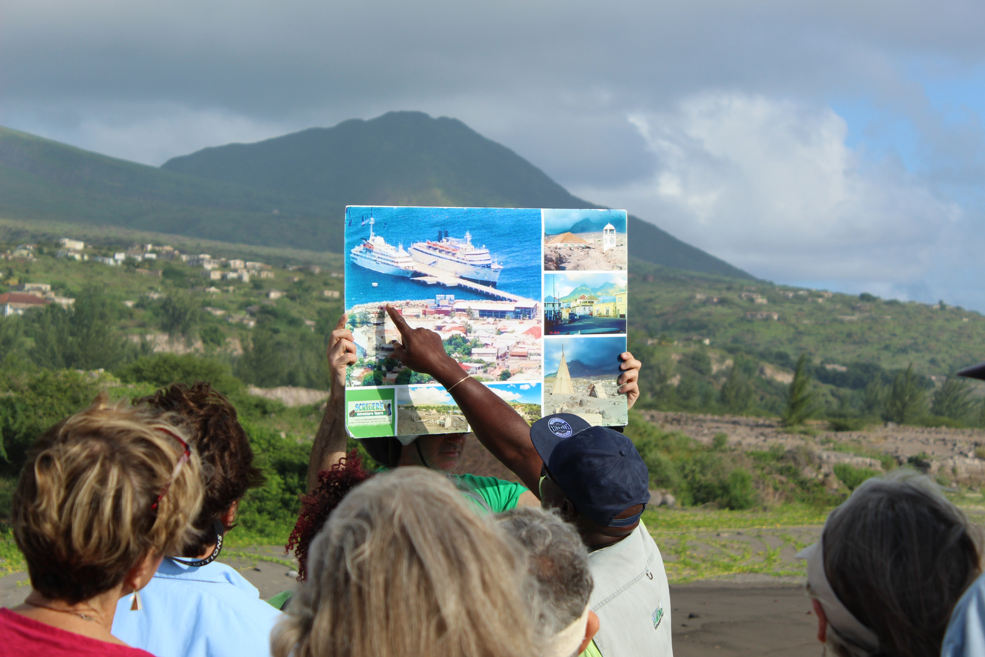 Scriber holding a photo board of Plymouth as guests look out toward the Soufrière Hills volcano